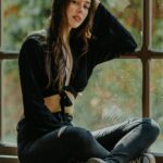 Fashionable young woman sitting by a window in casual attire, exuding confidence and style.